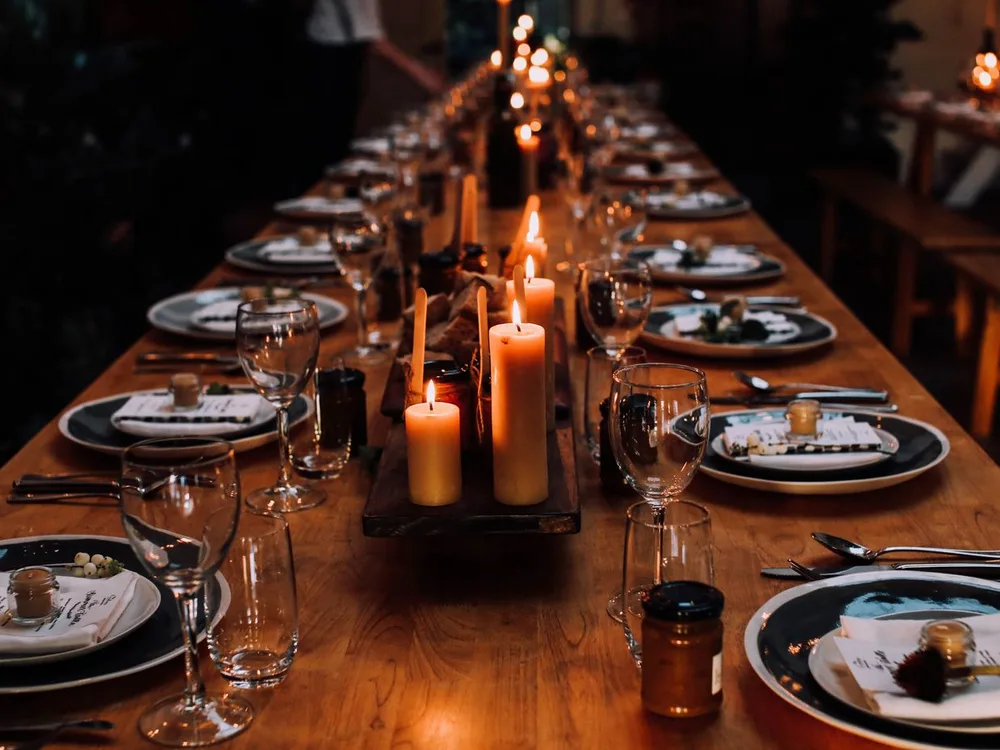 Mesa larga de banquete a la luz de las velas, con la vajilla montada sobre madera cálida