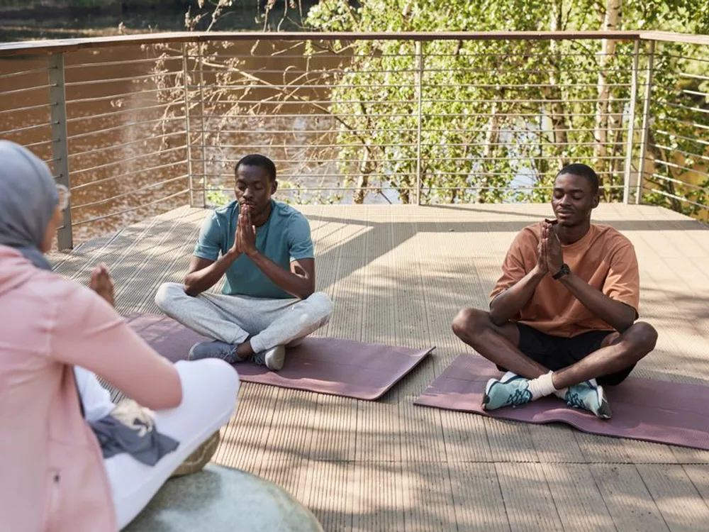 Personas meditando sentadas sobre esterillas en un deck de madera junto al agua